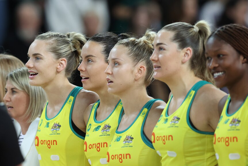 Australian netball players stand in a line and sing with smiles on their faces