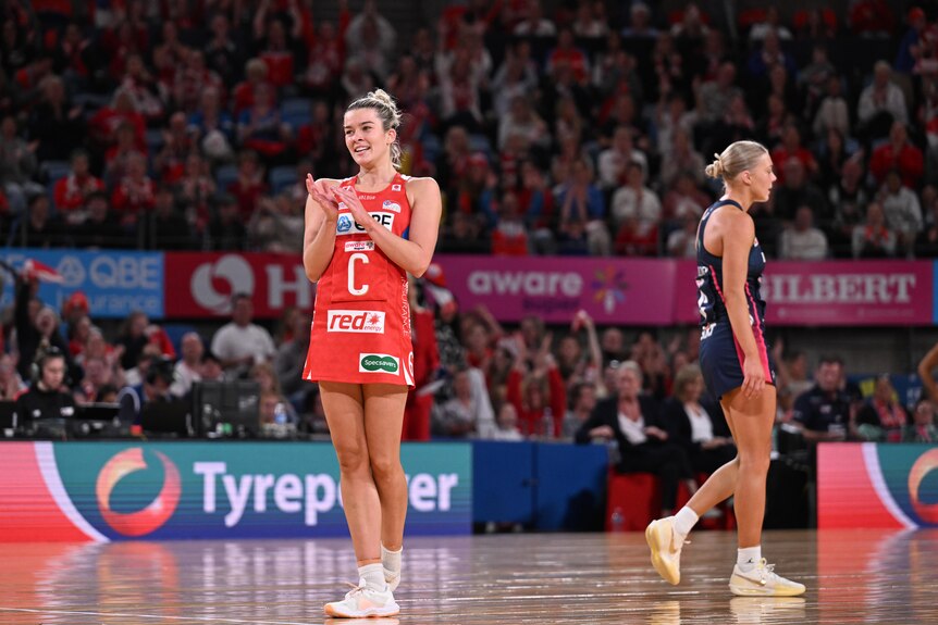 A player stands on court and claps in front of a crowd after her team wins