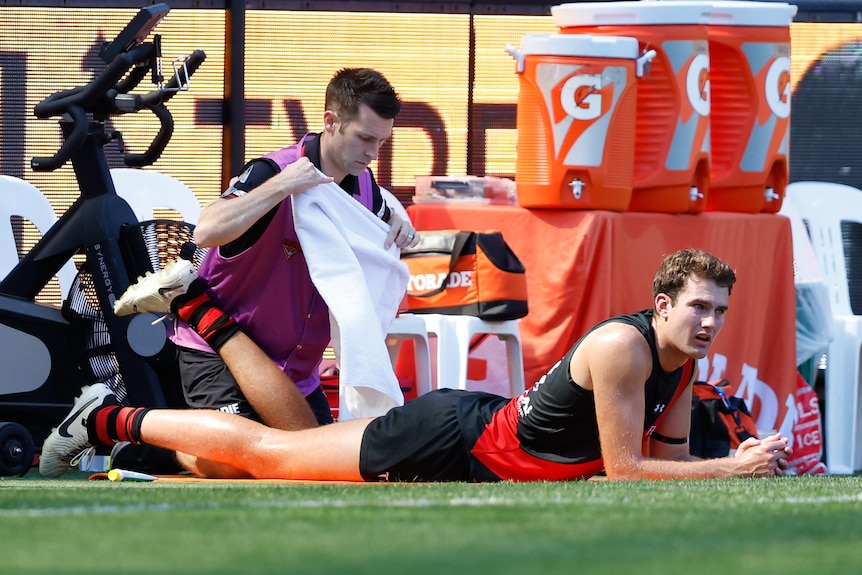 Zach Reid lays on his stomach on the boundary line while a trainer looks at his leg