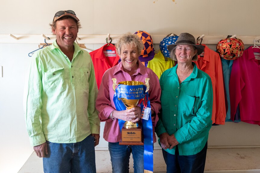 Two women and one man smiling and holding a large gold cup with ribbon on it that reads Brunette Downs