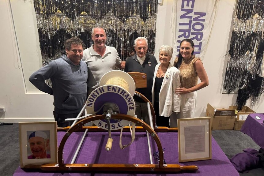 Three men and two women standing in front of a shiny background.