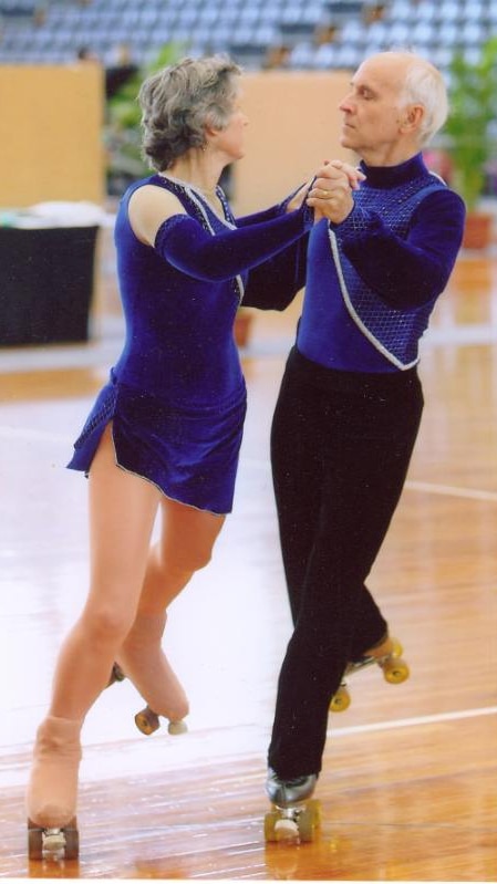 An older man and woman roller skate in blue outfits.