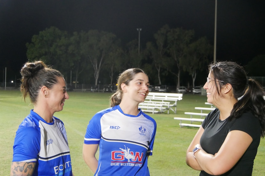 Three women standing together laughing at football training during the evening.