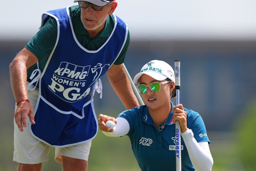 Minjee Lee and her caddie Michael Paterson crouch on a green and discuss a golf putt