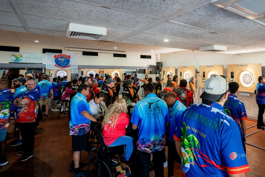 A function room filled with people. The walls are lined with dartboards. 