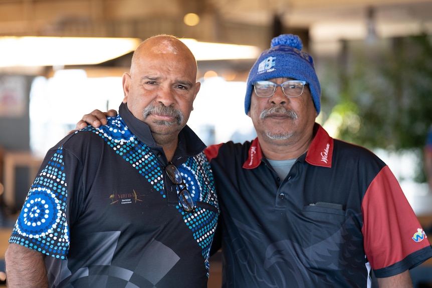 Two men stand next to each other with their arms around their shoulders.