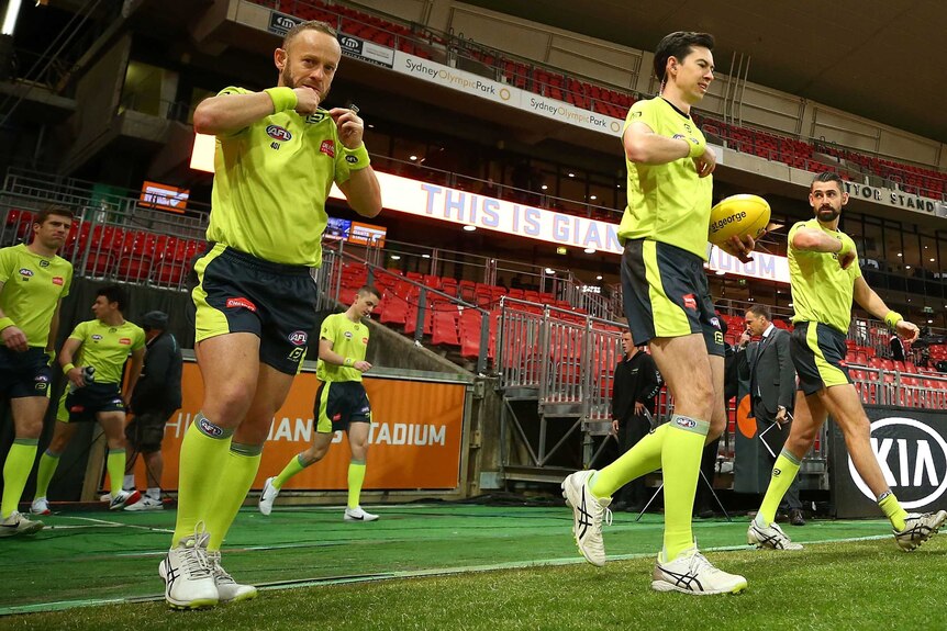 AFL umpires give signals as they step across the boundary line before a match.