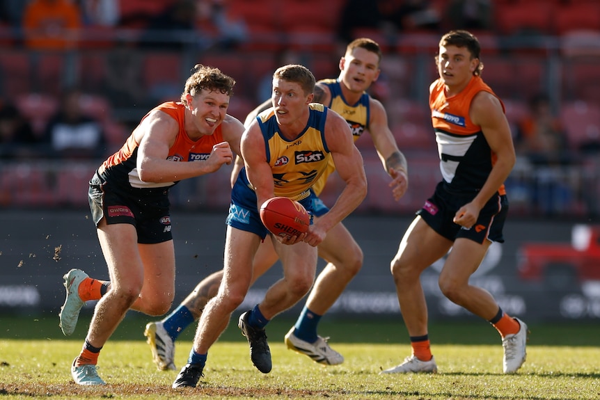 Matt Rowell holding an AFL ball surrounded by three other players during a game. 
