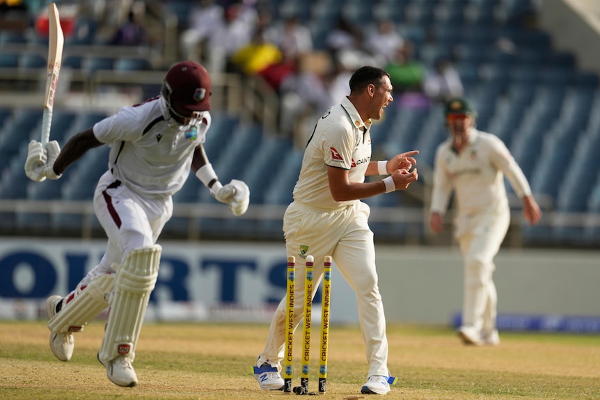 A cricketer behind the stumps holds his fingers out as a batter runs beside him.