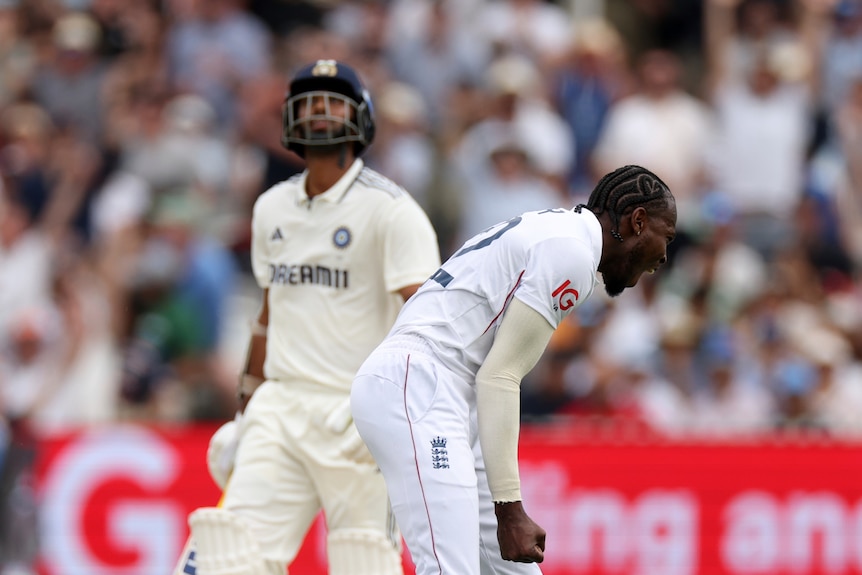 An England Test fast bowler bends over and yells in celebration after a wicket, as an Indian batsman walks off behind him. 