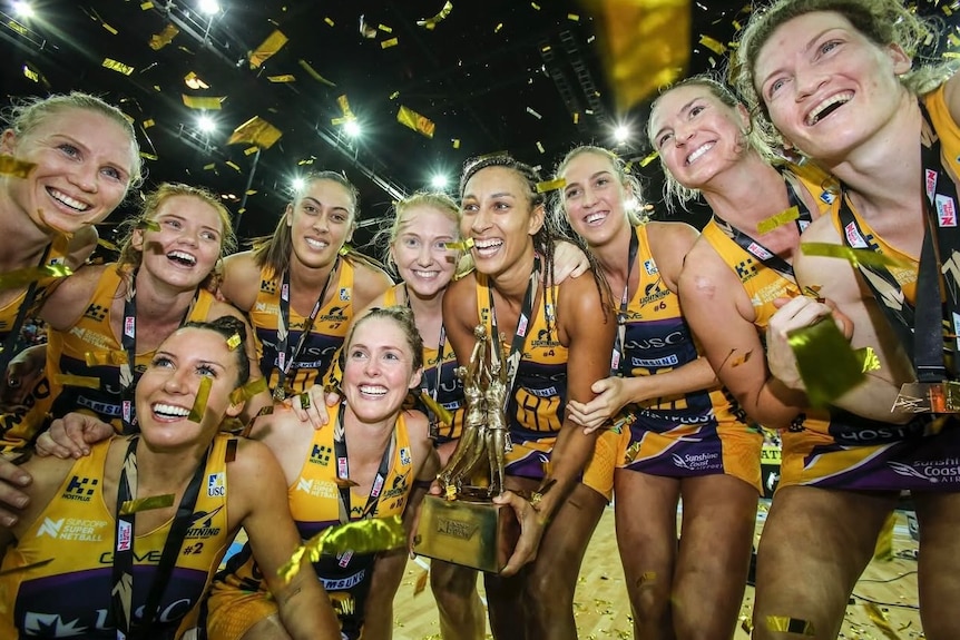 A team of netball players huddled around a trophy