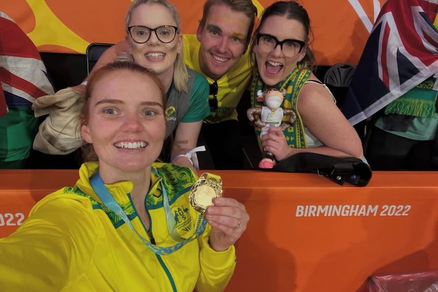 A woman poses with her gold medal in front of two women and a man