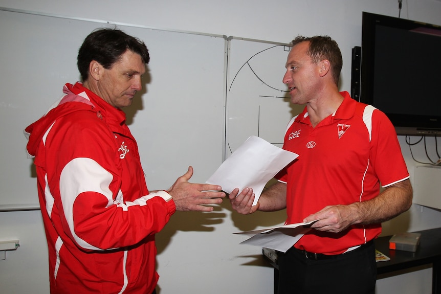 John Longmire passes a piece of paper to Paul Roos