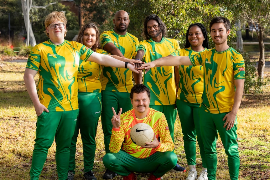 A team photo with players wearing green and gold kit and putting their hands in a circle.