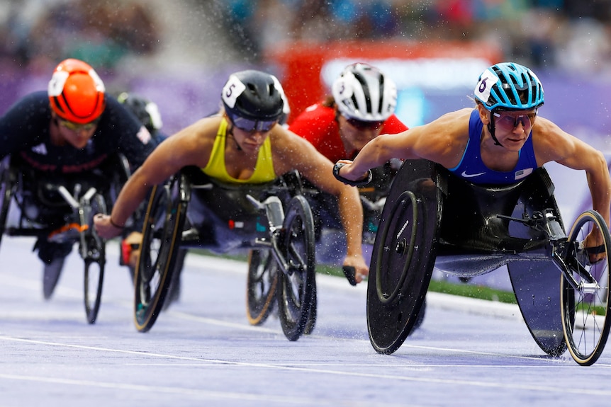 Female wheelchair racers push to the finish line on the track.
