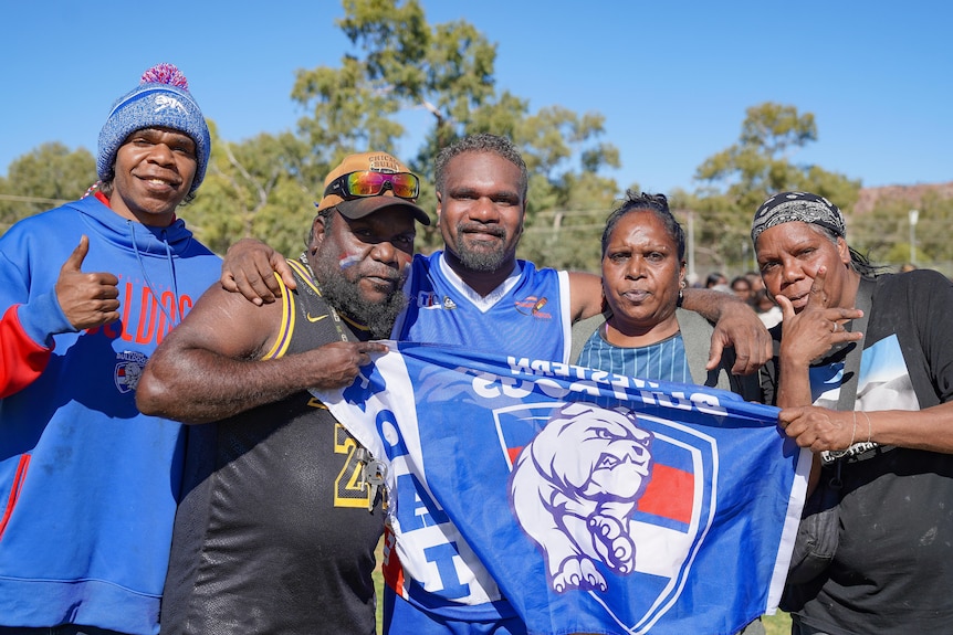 A uniformed football player standing with loved ones who are wearing club merch and holding a Bulldogs flag.