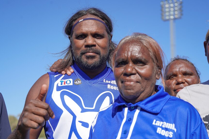 A football player smiling and giving a thumbs up as he stands alongside family members.