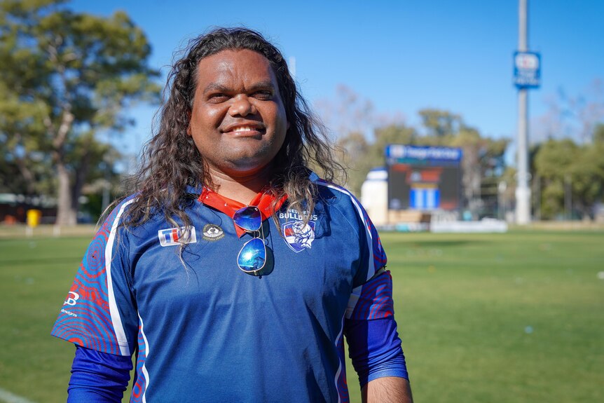 A man wearing his team's colours, smiling as he stands on a football field.