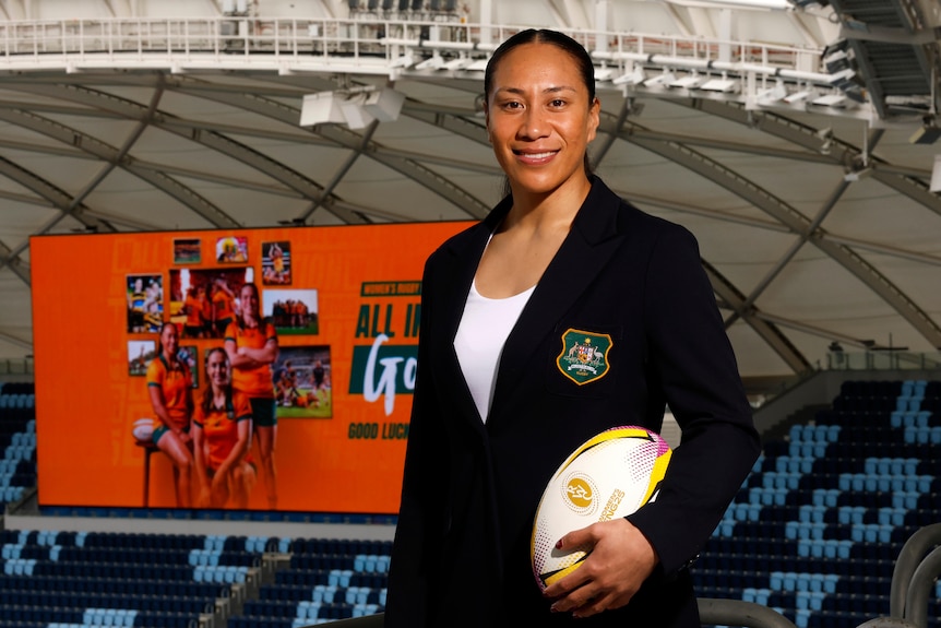 Wallaroos captain Siokapesi Palu stands in front of a Wallaroos sign in the background, she's wearing a blazer and holding ball