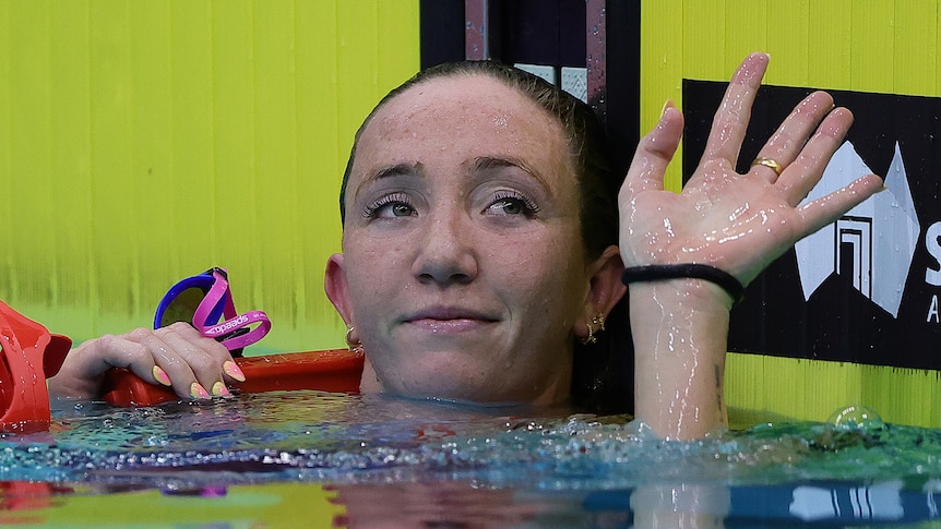 Australian swimmer Lani Pallister in the pool raises her hand to acknowledge the crowd after a race.
