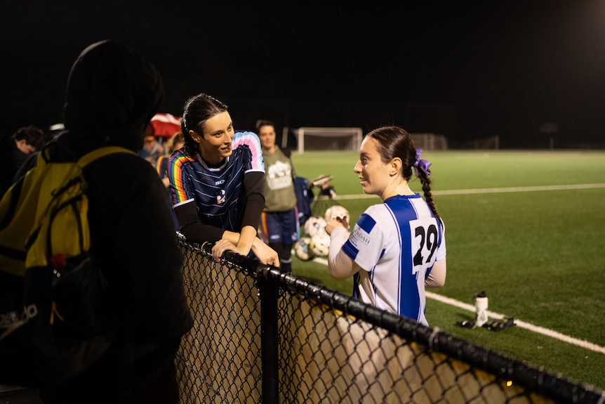 Woman on a soccer field with other players at night time having a chat.