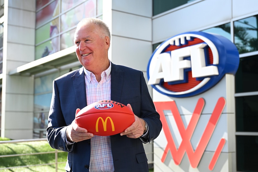 Greg Swann poses with a football in front of AFL House