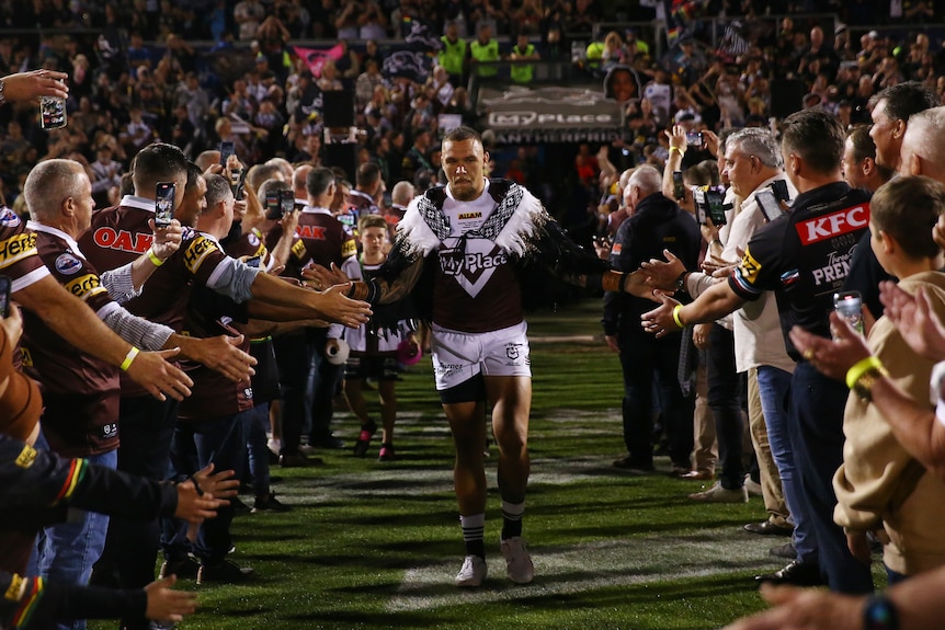 A man walks through a group of fans before a rugby league match 