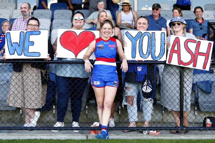 A Bulldogs AFLW player smiles as she stands behind a group of fans holding signs saying "We [heart] you Ash".