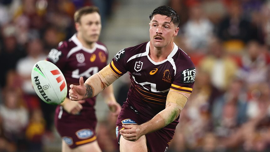 A Brisbane Broncos player spins the ball to his right as he tries to pass to a teammate.