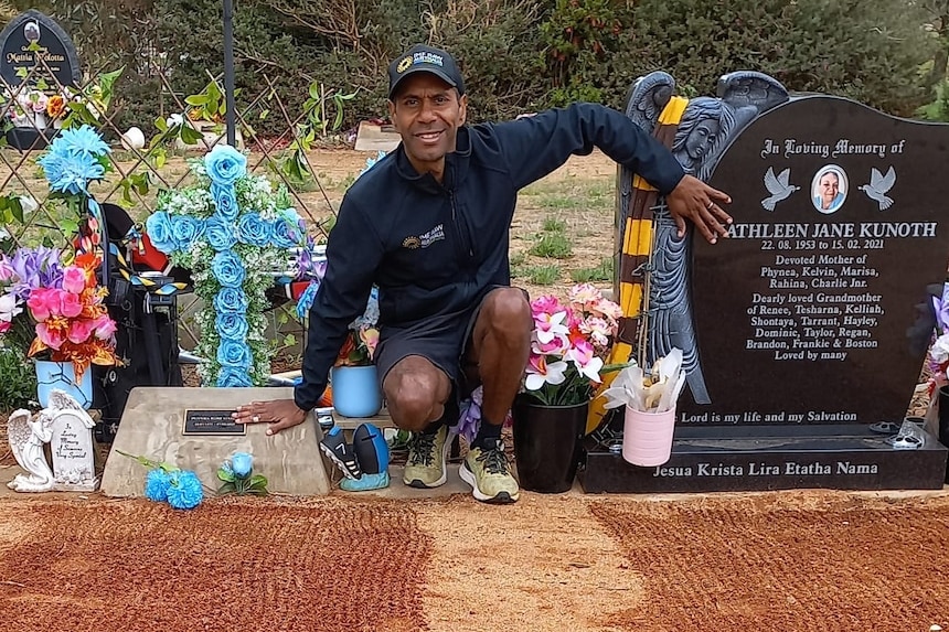Man kneeling next to the graves of his mother and sister. 