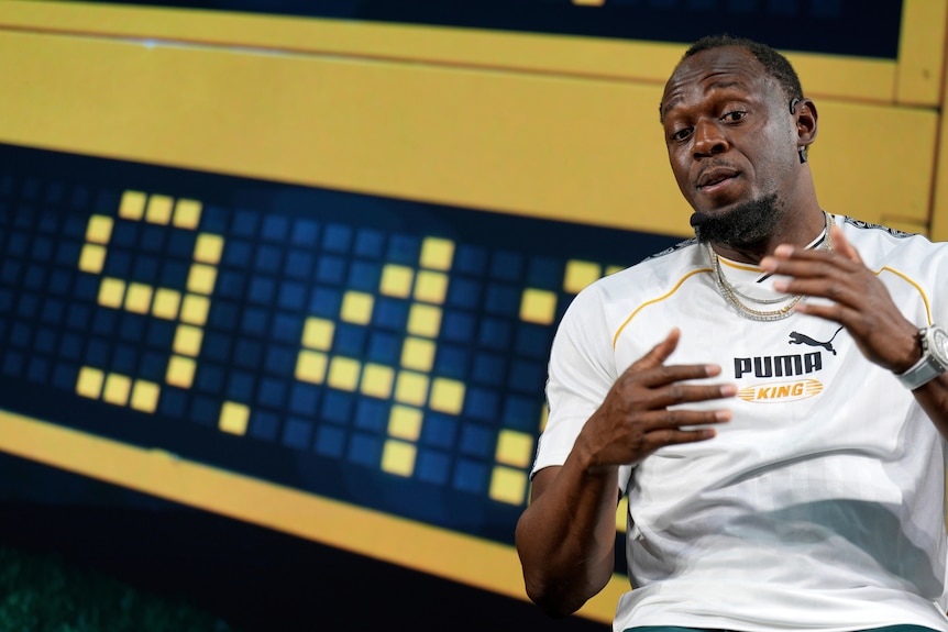 Former sprinter Usain Bolt stands in front of an athletics time clock at a press conference.