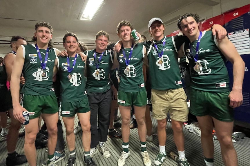 Six men in green football uniform stand with their arms around each other.