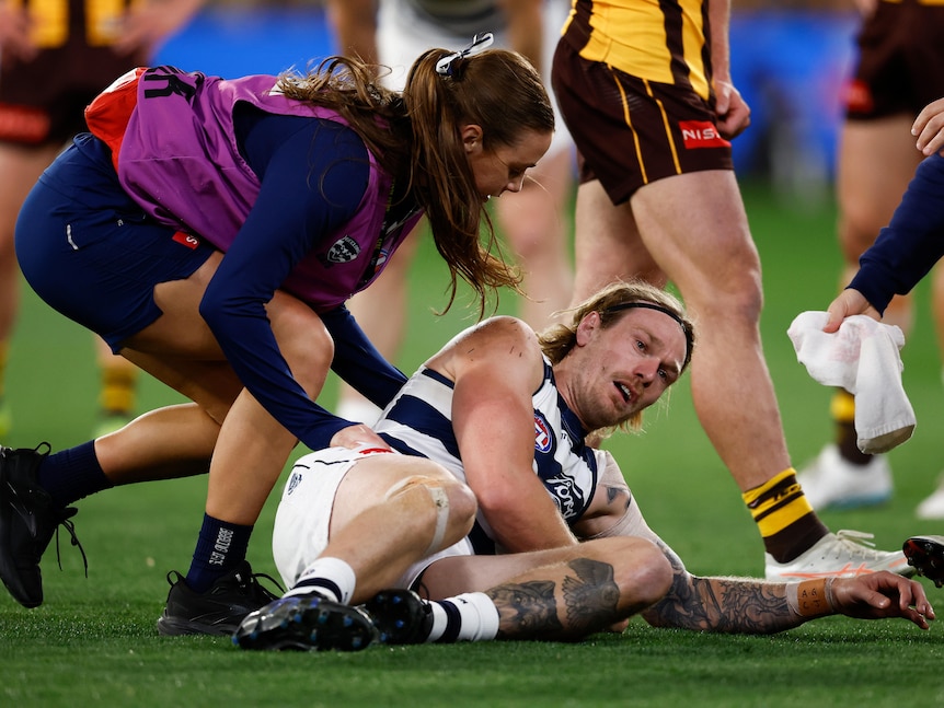 A dazed Geelong player lies on the ground as a medical officer checks on him at the MCG. 