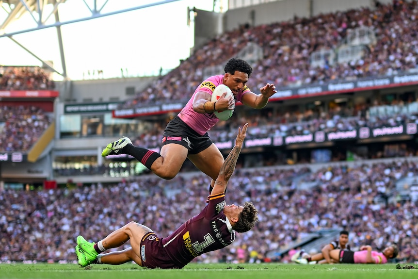 Paul Alamoti jumps over Reece Walsh in a Penrith-Brisbane NRL game.