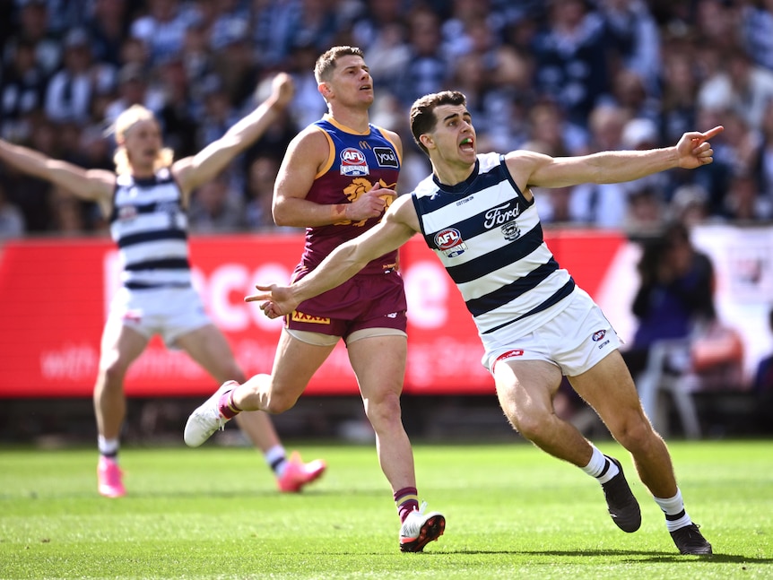 A Geelong AFL player runs away from goal with arms spread wide in celebration.