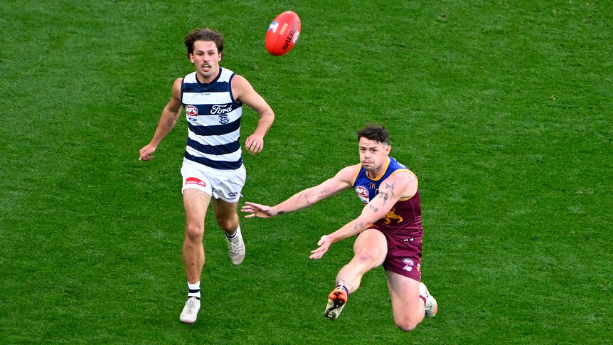 A Brisbane Lions player is pictured mid-kick as he launched the ball towards goal, with a Geelong player trailing behind.