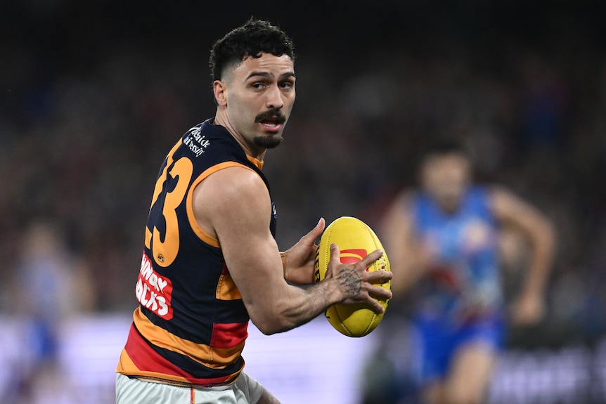 Izak Rankine of the Adelaide Crows holding the AFL ball in two hands, looking for a teammate