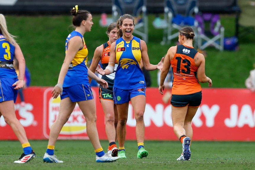 An AFLW player celebrates with arms outstretched