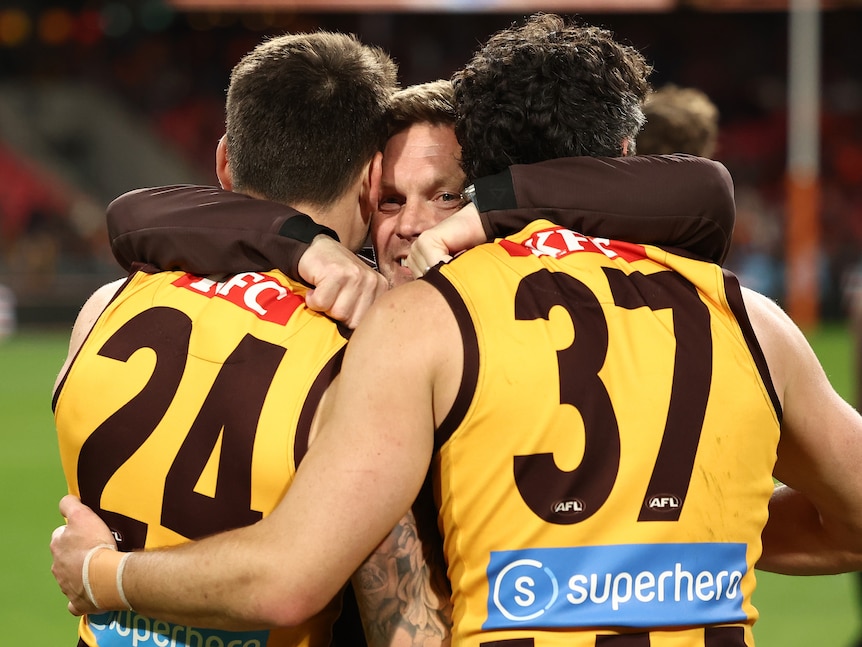 Hawks coach Sam Mitchell embraces Josh Battle and Tom Barrass after a final