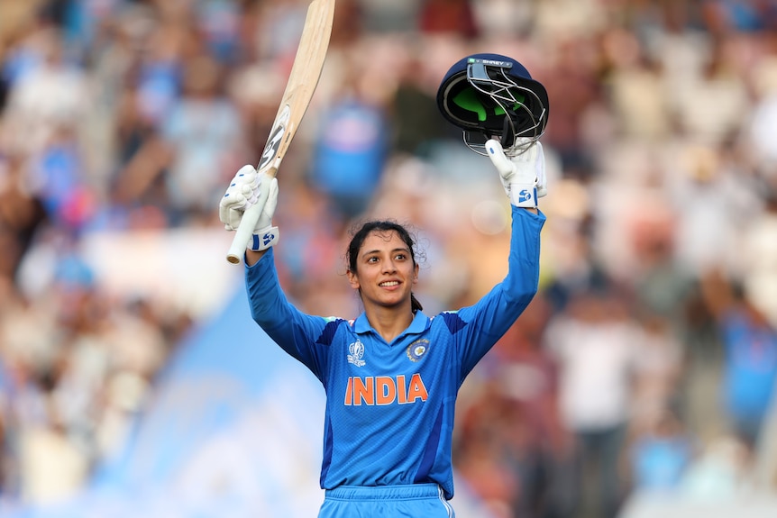 Smriti Mandhana holds her bat and helmet aloft in celebration