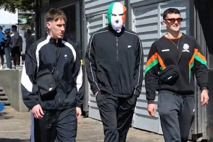 Three men in tracksuits, one with an Irish flag face mask.
