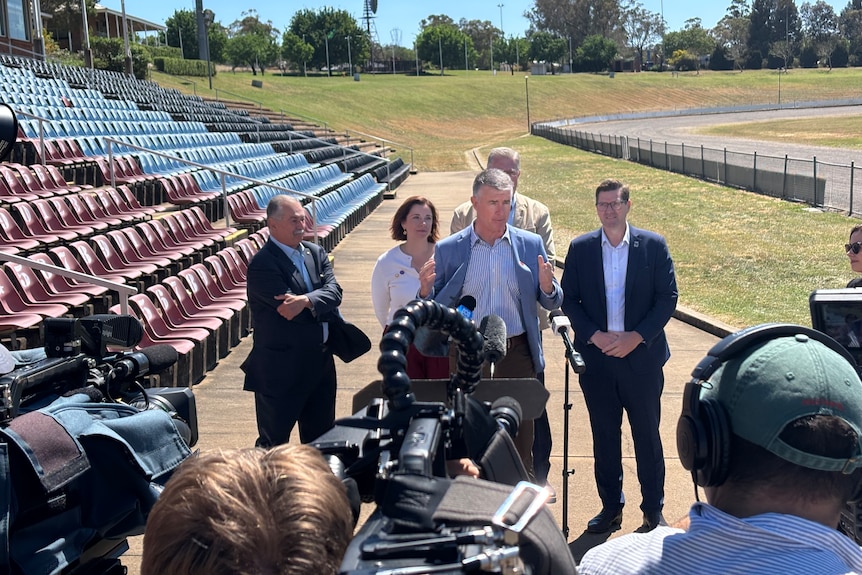 Five people standing in an outdoor arena in front of microphones