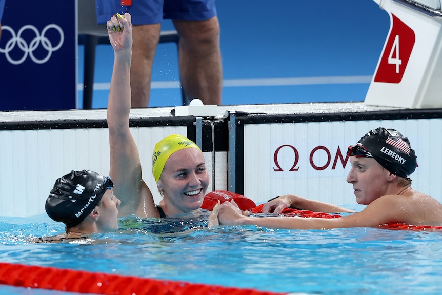 Ariarne Titmus holds up her hand as Katie Ledecky and Summer McIntosh look at each other