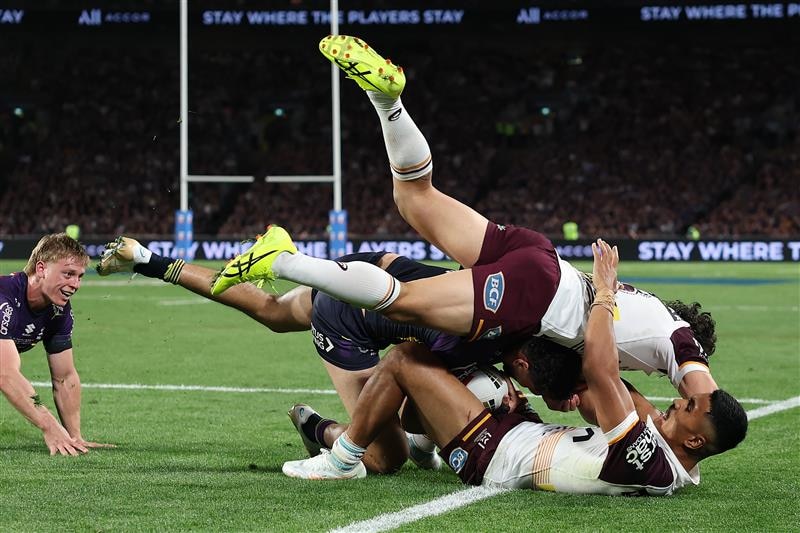Xavier Coates is tackled over the sideline by a pair of Broncos defenders