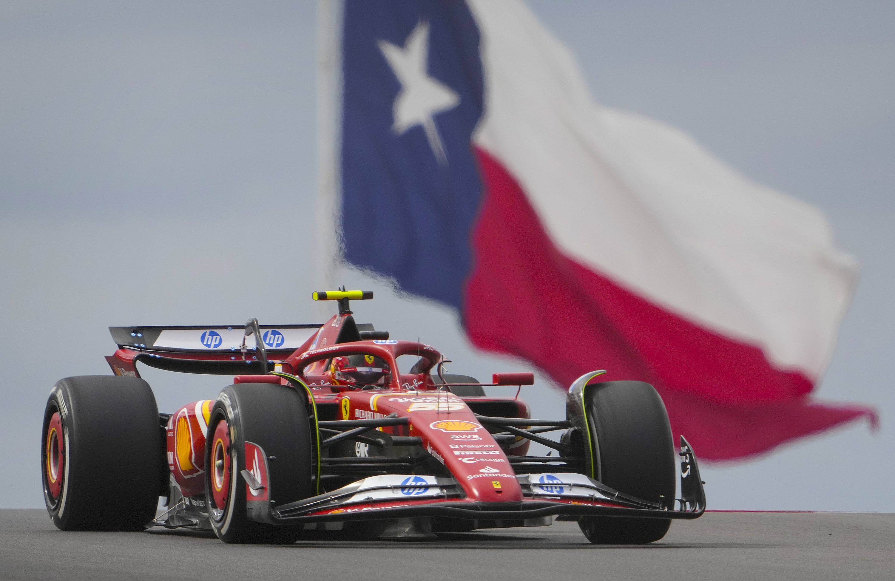 Ferrari F1 car comes over a rise, with a big Texas state flag in the background