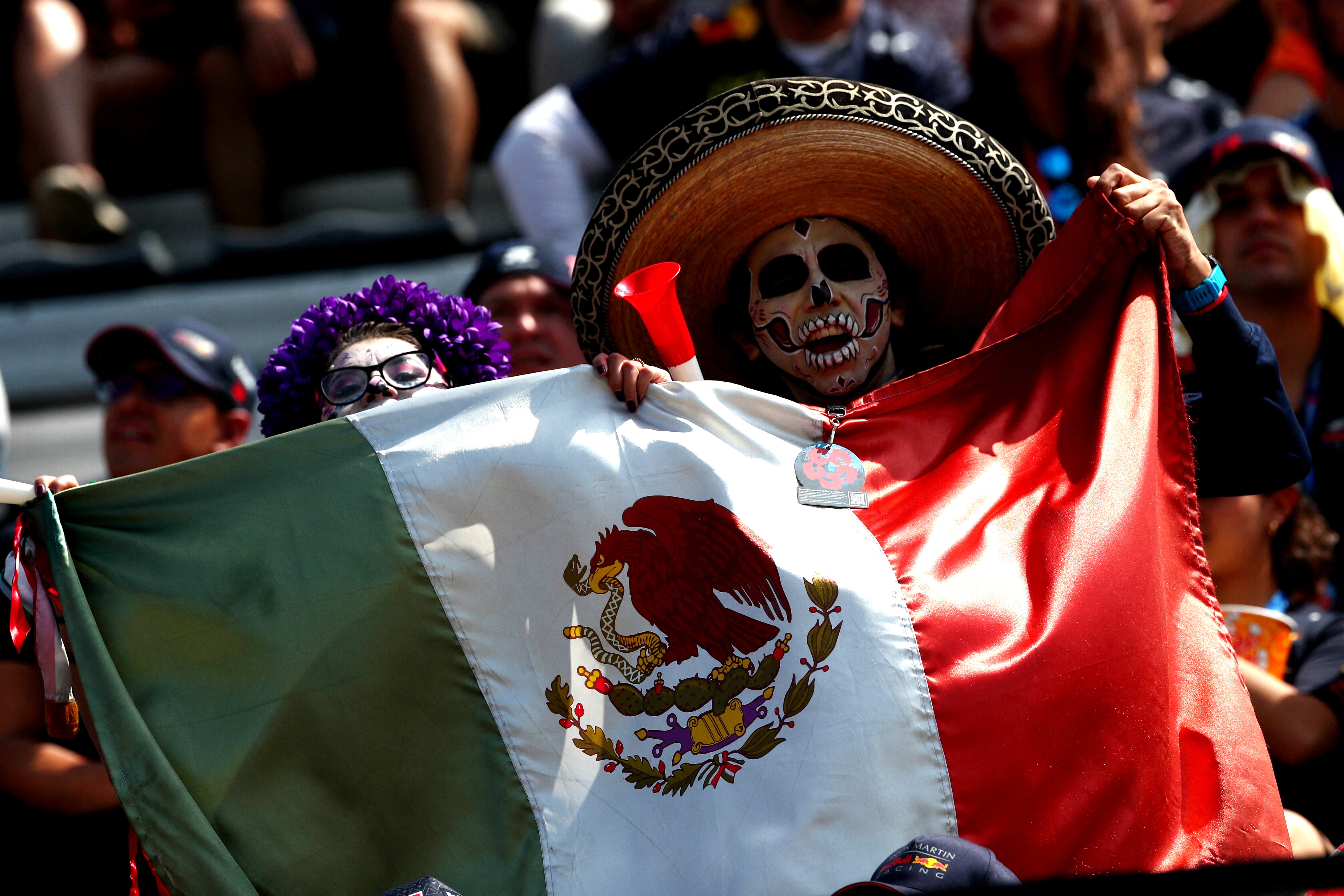 A fan dressed in a wrestling mask, holding a Mexican flag, at an F1 race