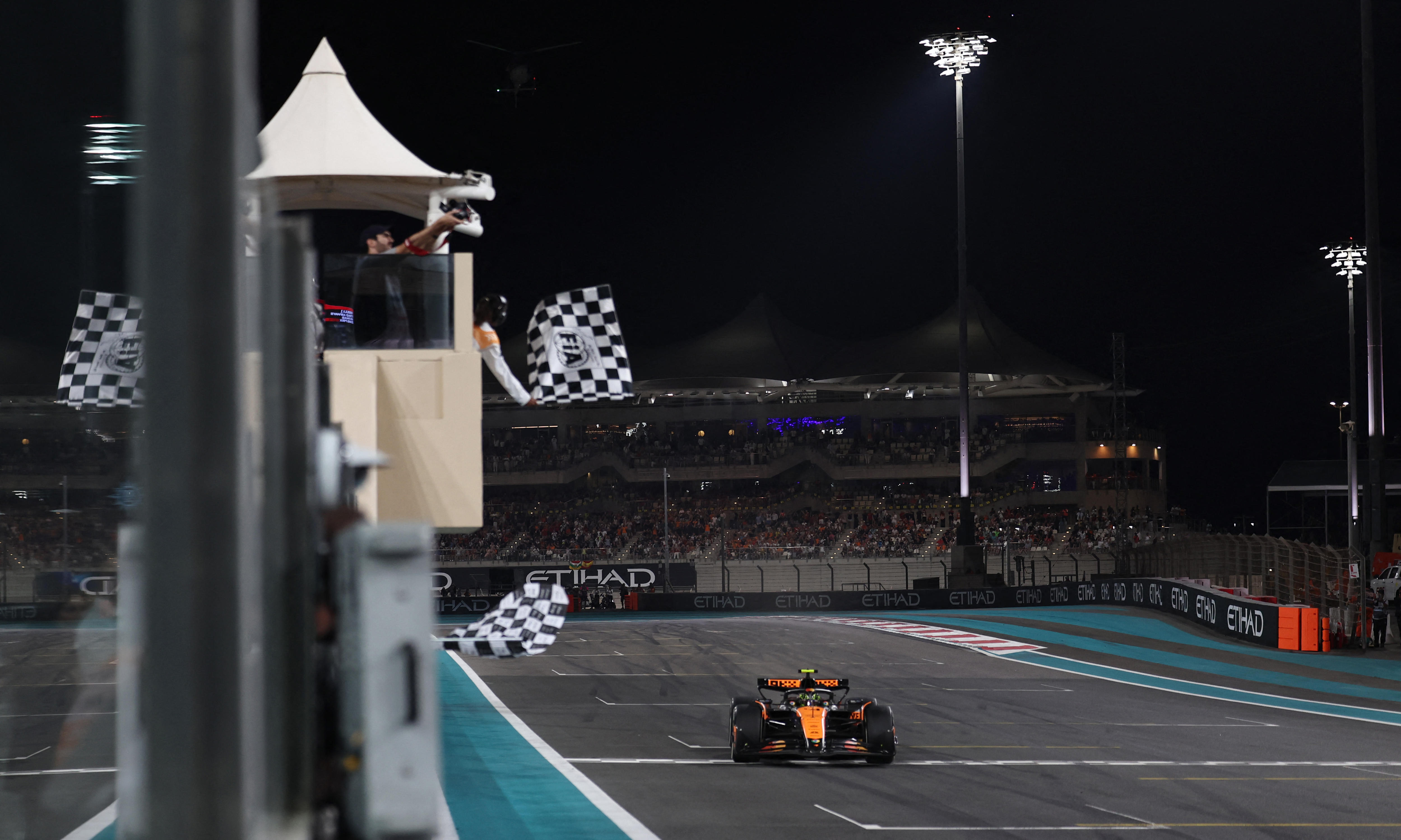 Lando Norris, in his McLaren F1 car, crosses the line with chequred flags waving.