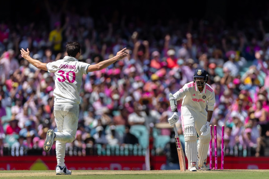 A cricketer celebrates a wicket, arms held high in the air while the batter is bowled