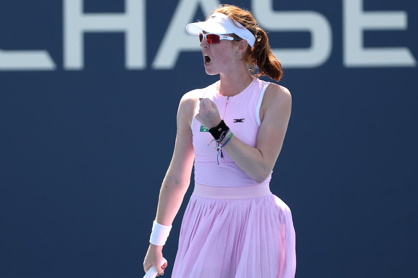 A young, female tennis player clenches her fist in triumph.