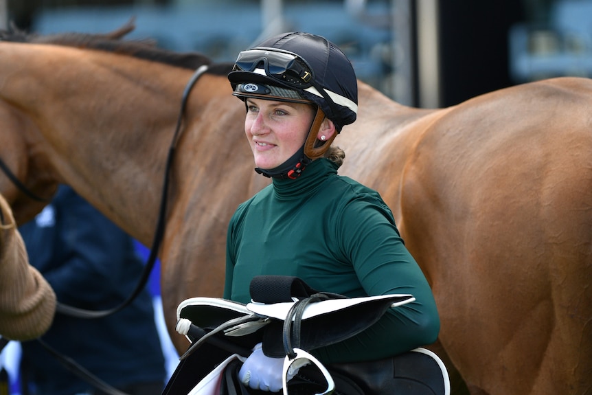 Female jockey standing in front of her horse 
